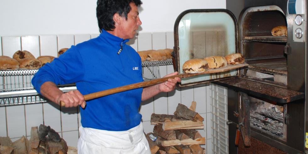 Brot wird mit dem Schießer in den Holzofen geschoben