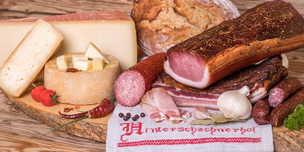 Speck, Käse und Bauernbrot vom Hinterschachnerhof auf einem Holzbrett mit besticktem Tuch